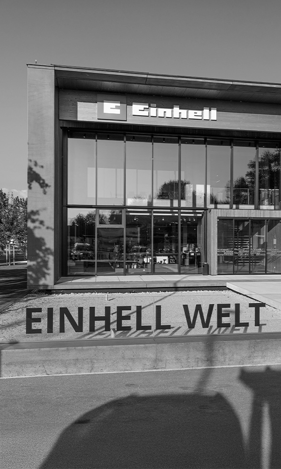 ภาพขาวดำของ Einhell world: อาคารบริษัททันสมัยพร้อมโลโก้ Einhell และพนักงานกลุ่มใหญ่