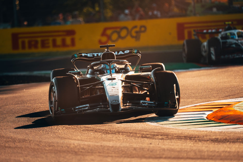 รถแข่งของทีม Mercedes-AMG PETRONAS Formula One Team กำลังวิ่งบนสนามที่มีแสงแดดระหว่างการแข่งขันกรังด์ปรีซ์ รถเข้าโค้งด้วยความเร็วสูง โดยมีรถอีกคันหนึ่งอยู่ด้านหลัง