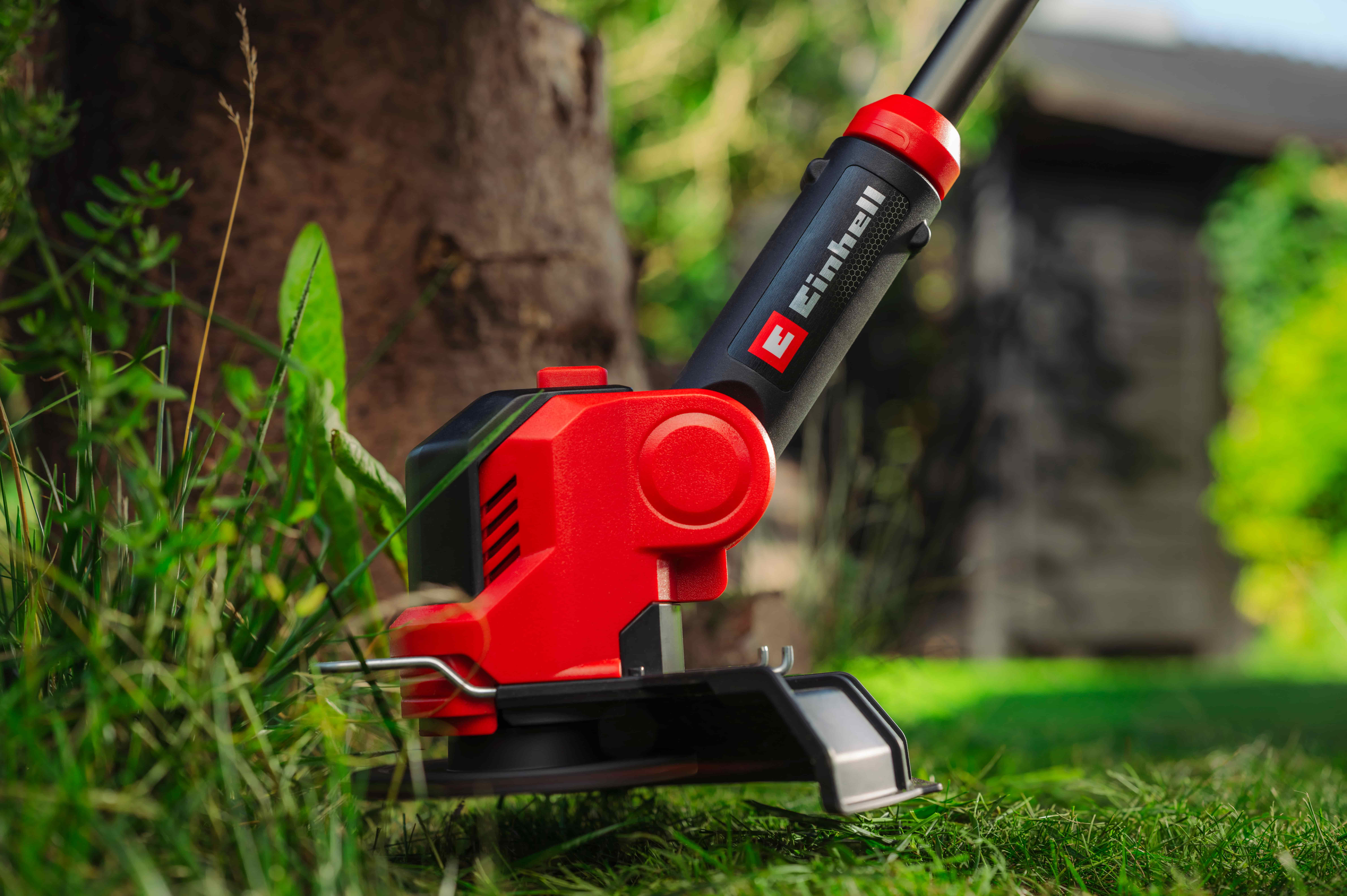 เครื่องตัดหญ้า Einhell กำลังตัดหญ้ารอบต้นไม้ในสวน