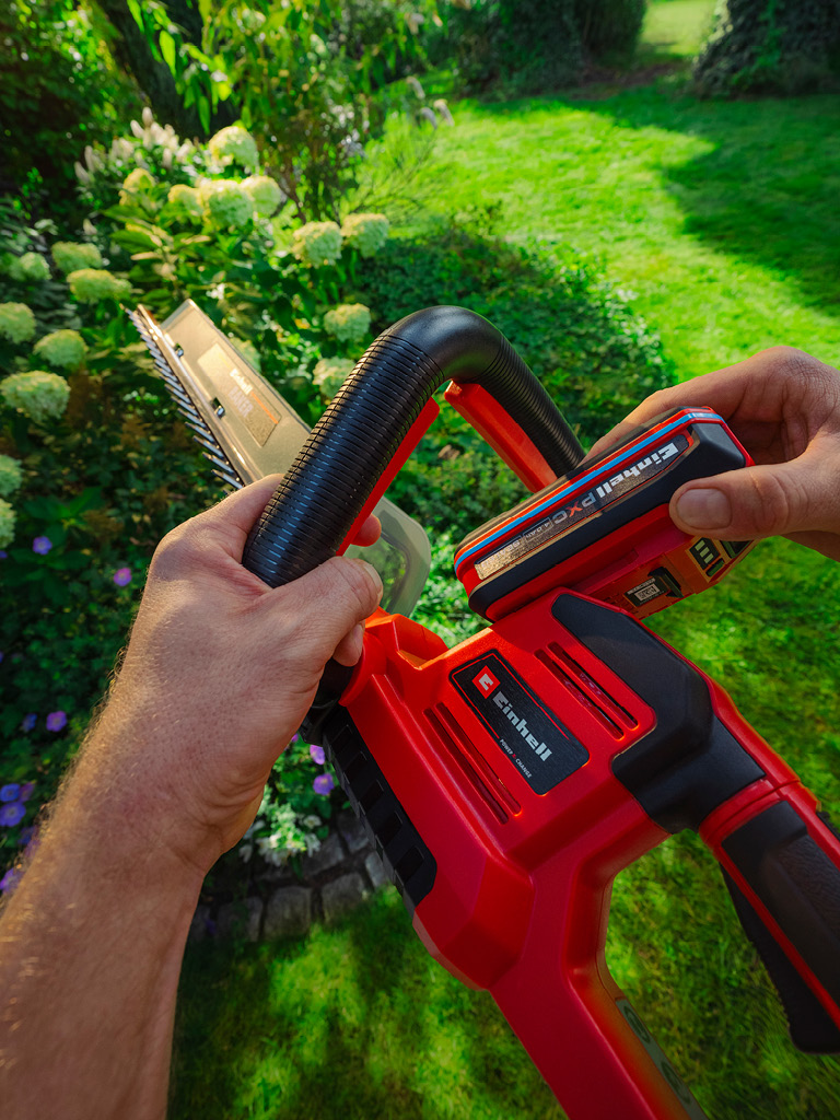 มือกำลังใส่แบตเตอรี่ Einhell เข้าไปในเครื่องมือทำสวน