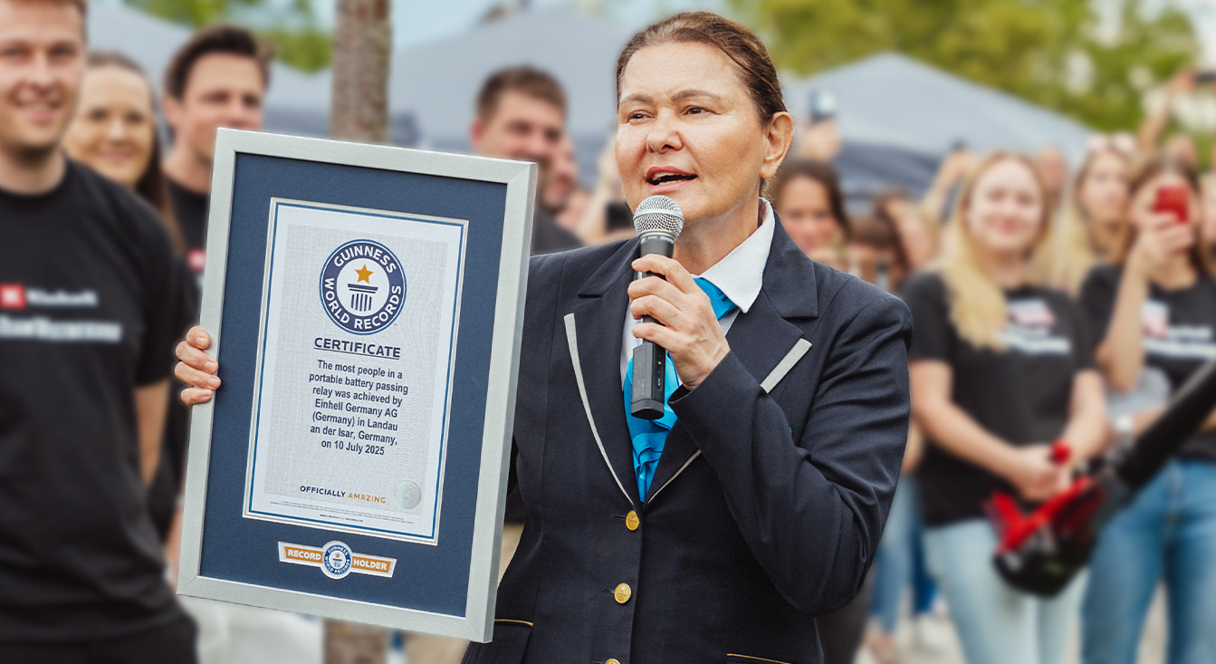 ผู้หญิงในชุดทางการของ Guinness ถือใบประกาศนียบัตรสำหรับสถิติโลกการส่งต่อแบตเตอรี่ของ Einhell