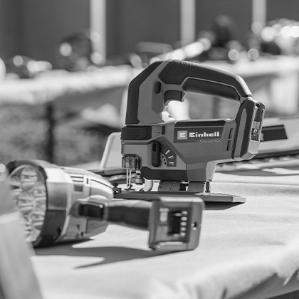 เลื่อยจิ๊กซอว์ไร้สาย Einhell ตั้งอยู่บนโต๊ะ ด้านหน้ามีไฟไร้สาย (ภาพขาวดำ)